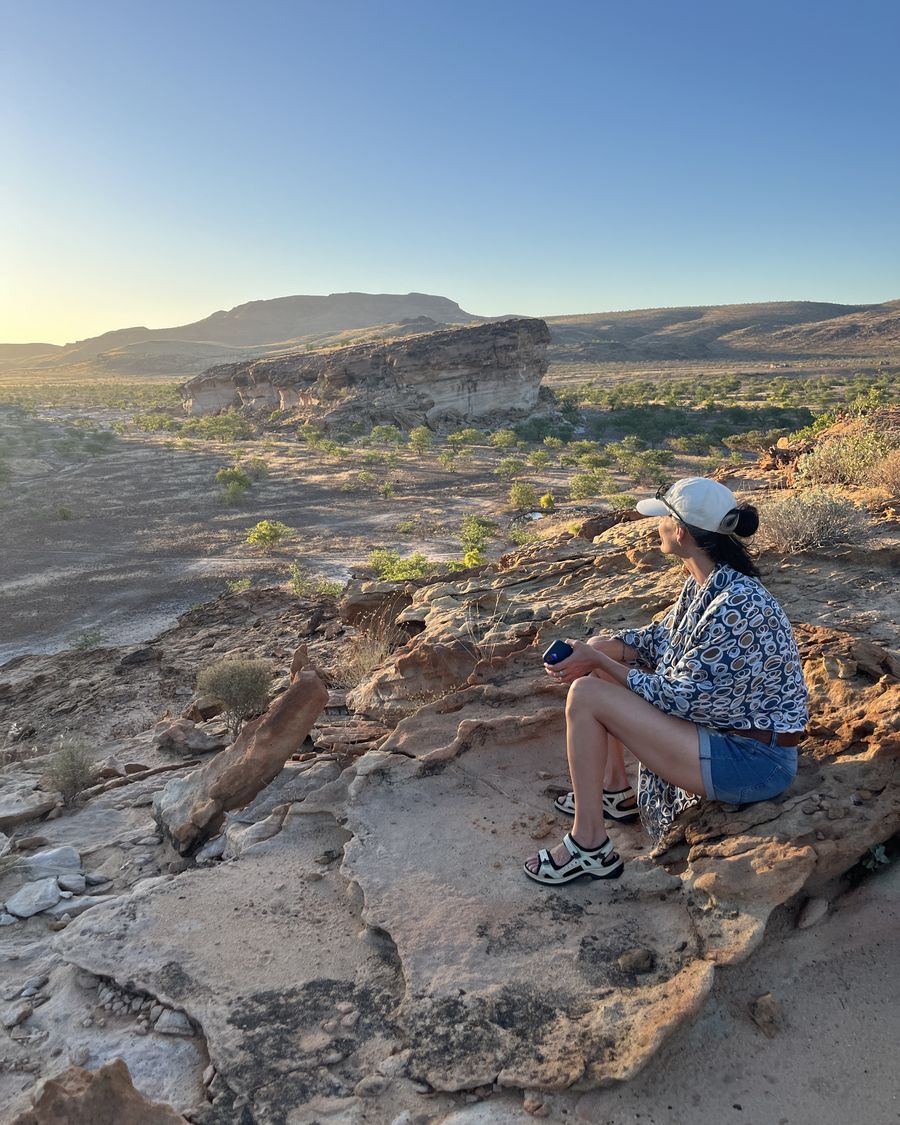 Kathleen Schütz sitzt in der Abendsonne auf Felsen in Namibia und blickt in die Landschaft